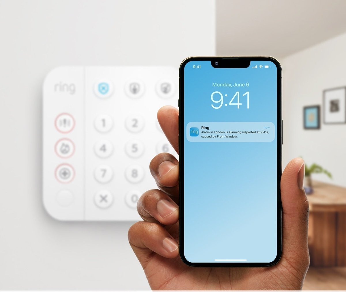 Ring Alarm keypad on a wall beside a phone showing a Ring alarm notification